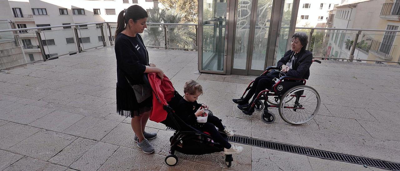 Marta Jaume, con su hija pequeña, Ariana, y Francisca Solivellas, ayer, esperando en vano a que  el ascensor de la plaza Major se pusiera en marcha. | MANU MIELNIEZUK