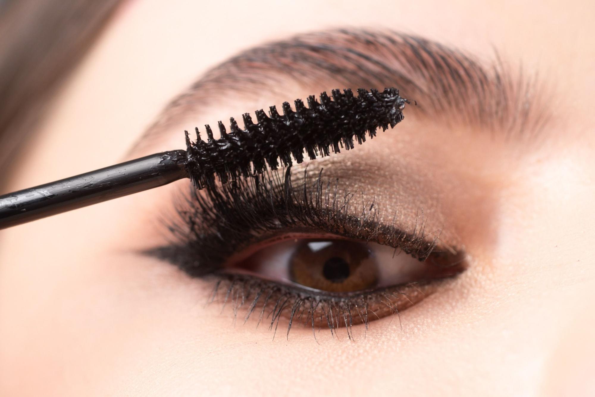 Closeup of eye makeup. Applying maskara on lushes Young woman getting make up with brush. Eyes visage woman.
