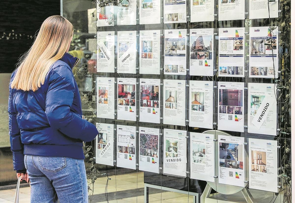 Una joven mira los anuncios de viviendas en el escaparate de una agencia inmobiliaria.