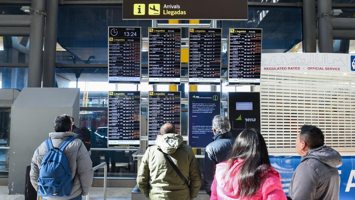 Varias personas observan los paneles informativos que anuncian retrasos de llegadas en algunos vuelos en Barajas.