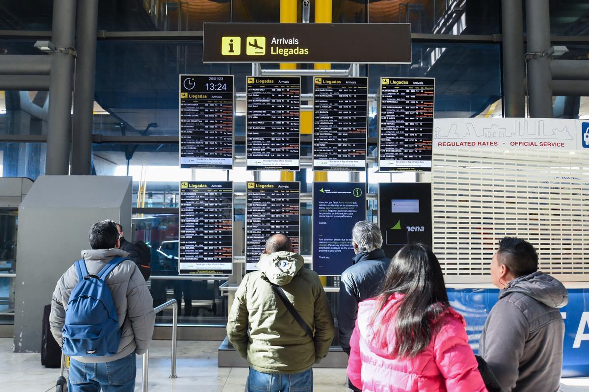 Varias personas observan los paneles informativos que anuncian retrasos de llegadas en algunos vuelos en Barajas.