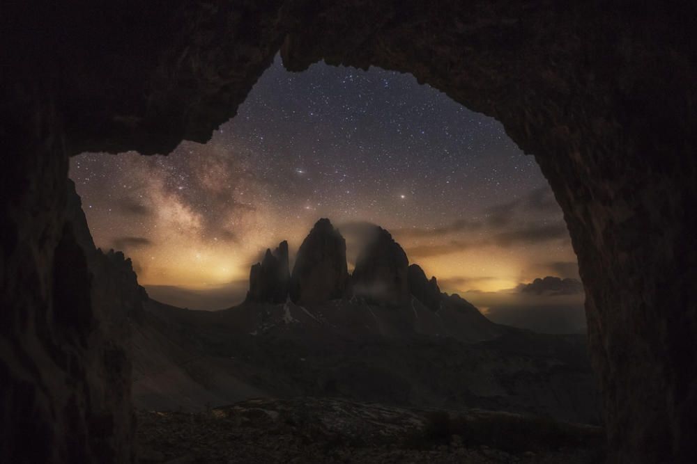 Visió nocturna dels Tres Cims de Lavaredo amb la via Làctia com a rerefons des d'una cova que ens retrotrau a altres temps