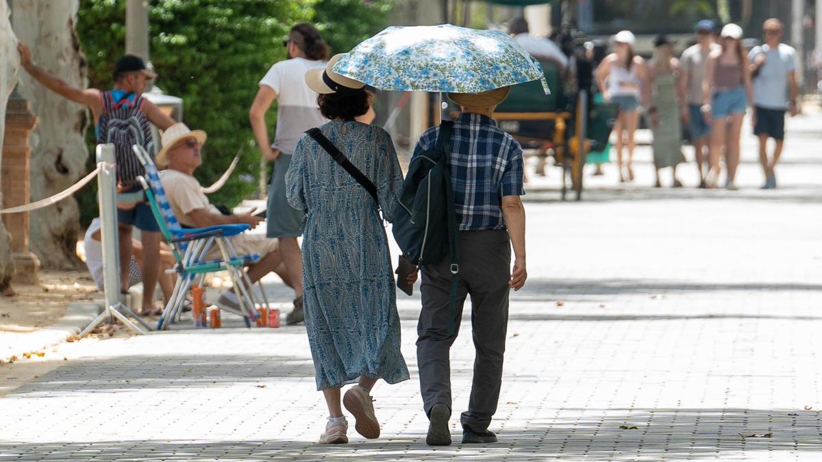 Una pareja pasea resguardada bajo un paraguas para mitigar los efectos del Sol en Sevilla.