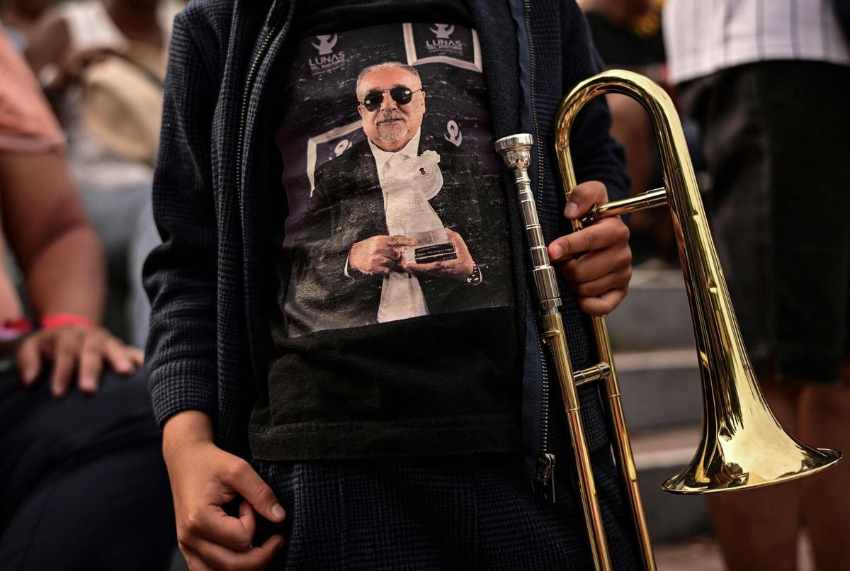 A child wearing a T-shirt depicting the late Willie Colon holds a trombone as he waits for the start of a tribute to the US musician in Panama City on April 12, 2026. US musician Willie Colon died in Bronxville, New York, on February 21, 2026, at the age of 75.
