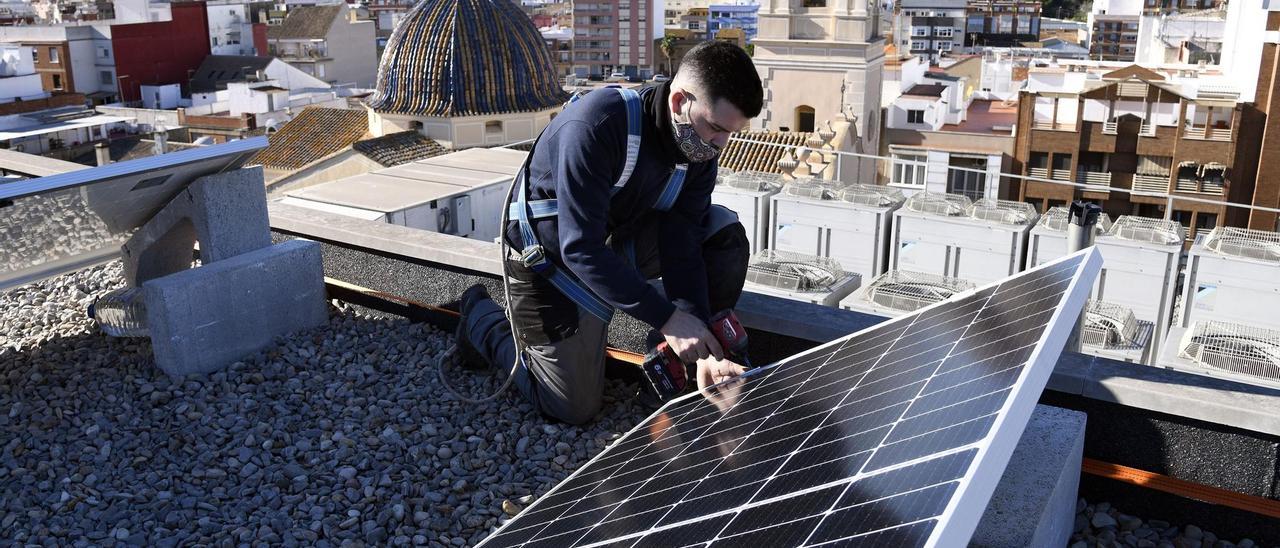 Un operador instala placas fotovoltaicas en un tejado de una vivienda en el núcleo urbano.