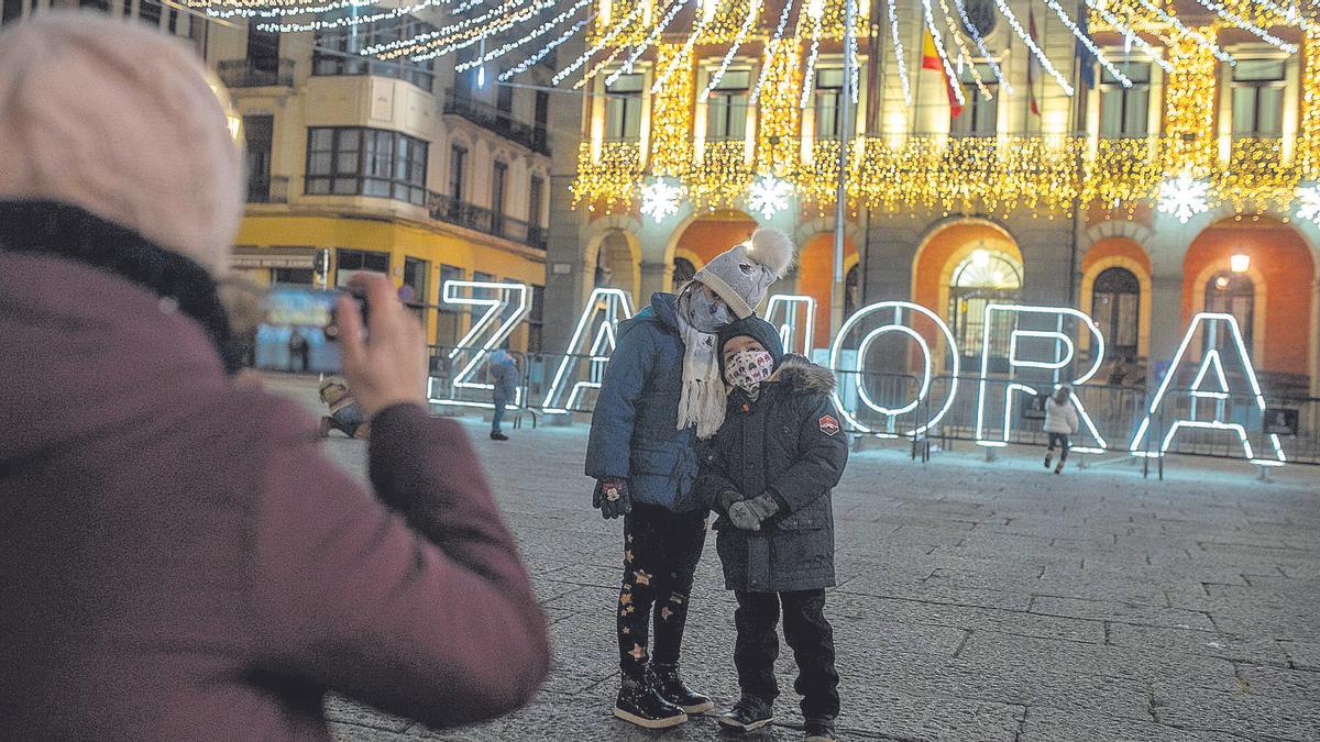 Una mujer hace fotos a dos niños con las luces de Navidad de la Plaza Mayor.