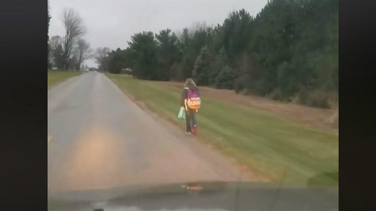 Imagen de la niña caminando por una larga carretera desde el interior del vehículo