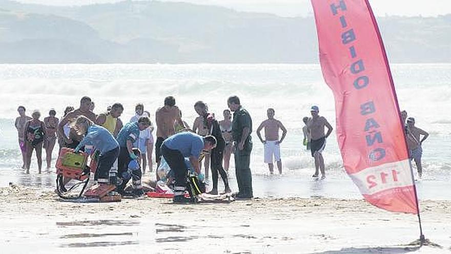 En la fotografía superior, profesionales sanitarios se preparan para reanimar a la víctima ante usuarios de la playa y un agente de la Guardia Civil. A la izquierda, aterrizaje en San Juan del helicóptero medicalizado del Principado.