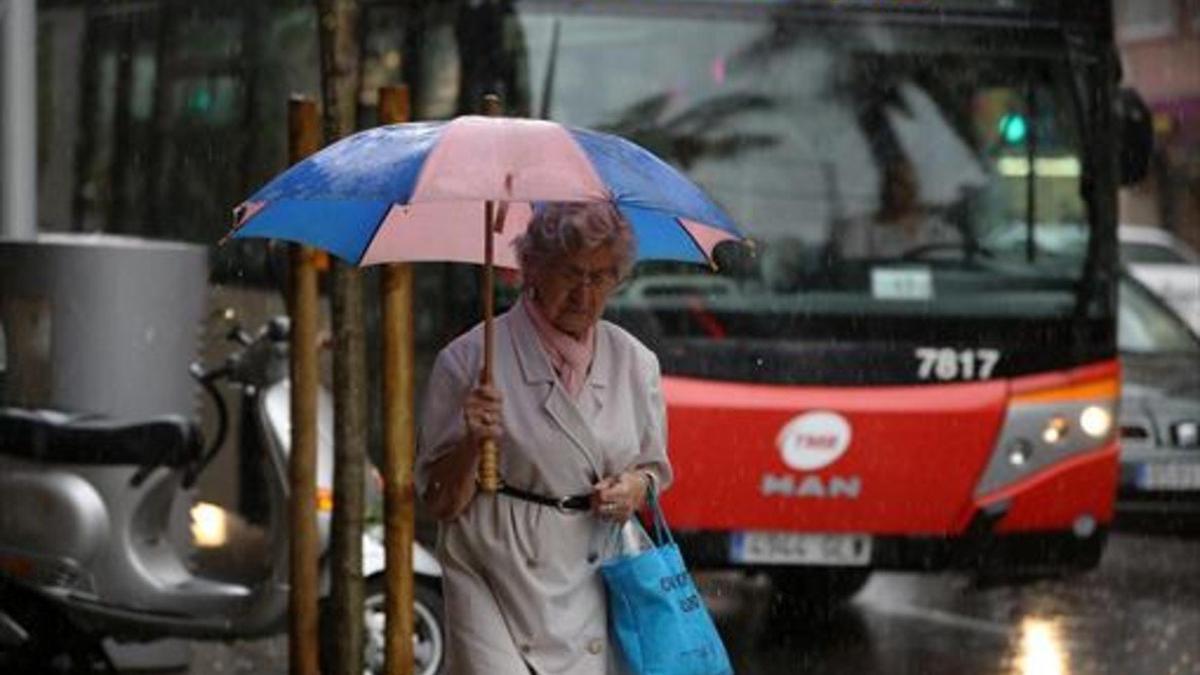Una mujer camina bajo la lluvia con gabardina y paraguas, en Barcelona.