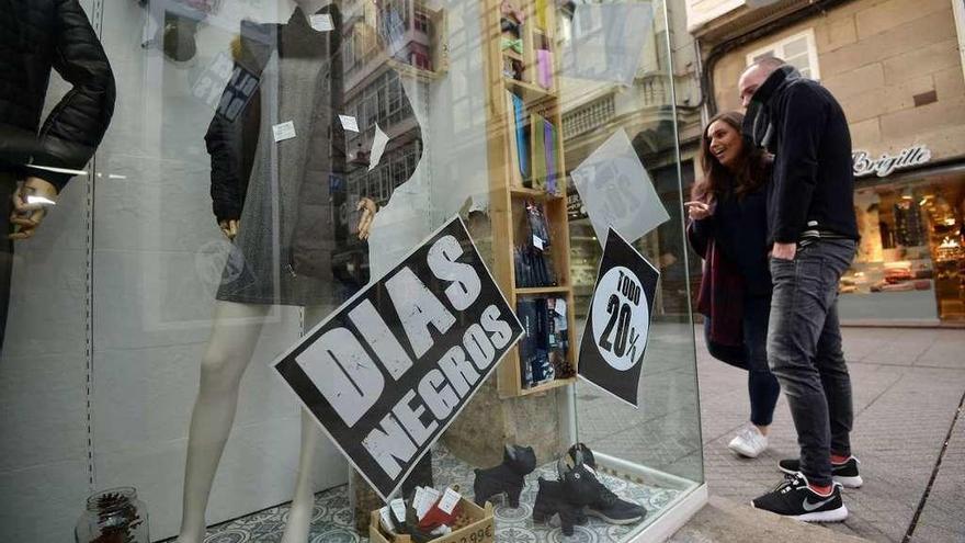 Dos jóvenes observan el escaparate de una de las tiendas de ropa que se suma al Black Friday. // G. Santos