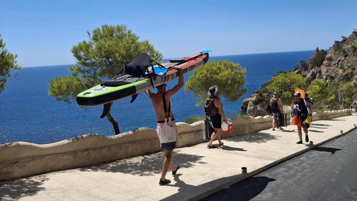 La imagen que se repite: un bañista baja a la cala del Moraig con la tabla sobre la cabeza