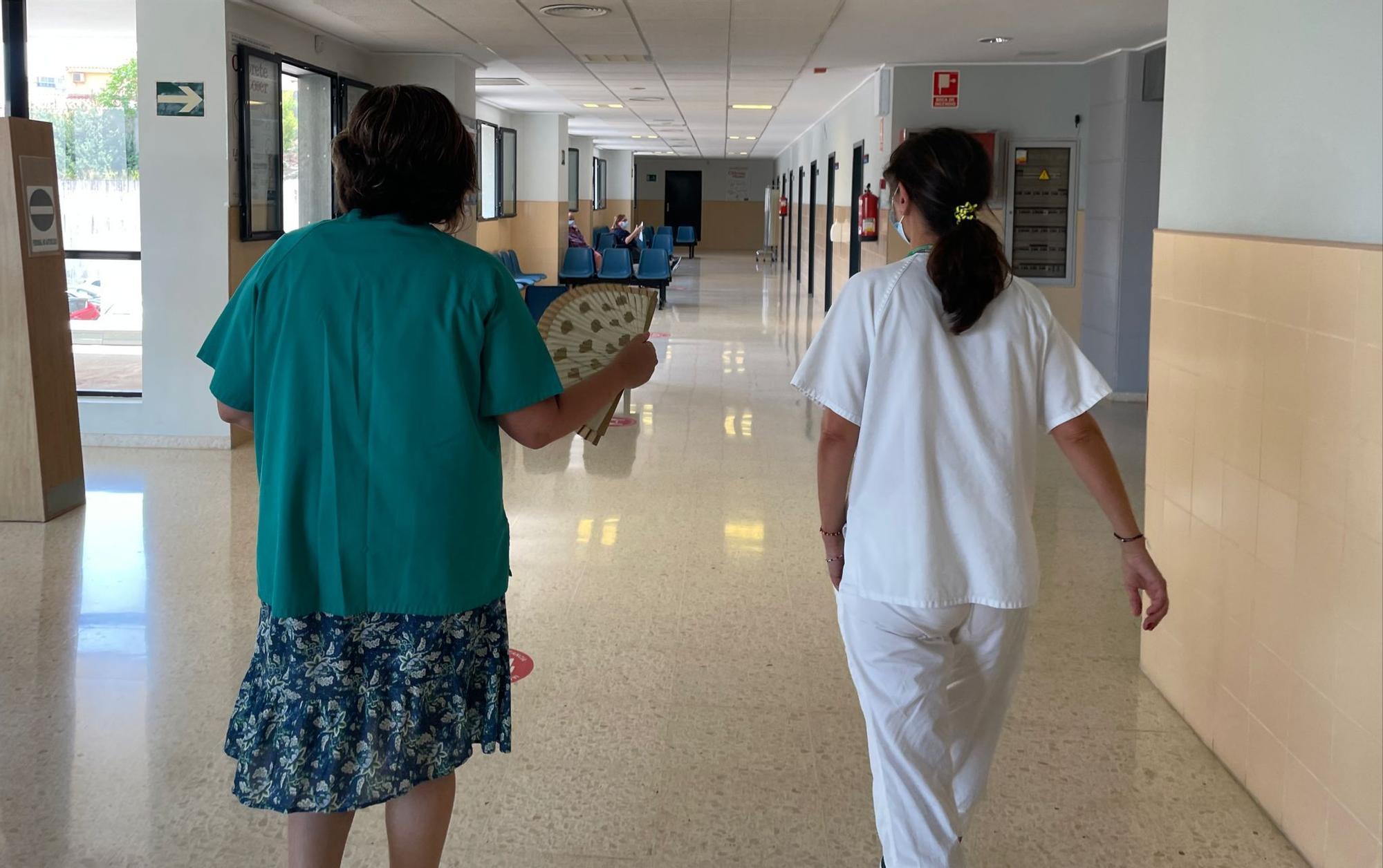 Dos sanitarias se desplazan por uno de los pasillos del Centro de Especialidades, una de ellas con un abanico por el calor. Al fondo se observa uno de los parabanes que se han colocado en las puertas de algunas consultas para poderlas tener abiertas y que corra el aire sin que el paciente sea visto desde fuera.