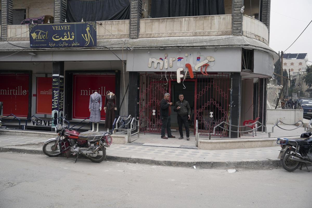Dos hombres toman cafe frente a un comercio afectado por la guerra, en la ciudad de Idlib.