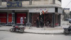 Dos hombres toman cafe frente a un comercio afectado por la guerra, en la ciudad de Idlib.