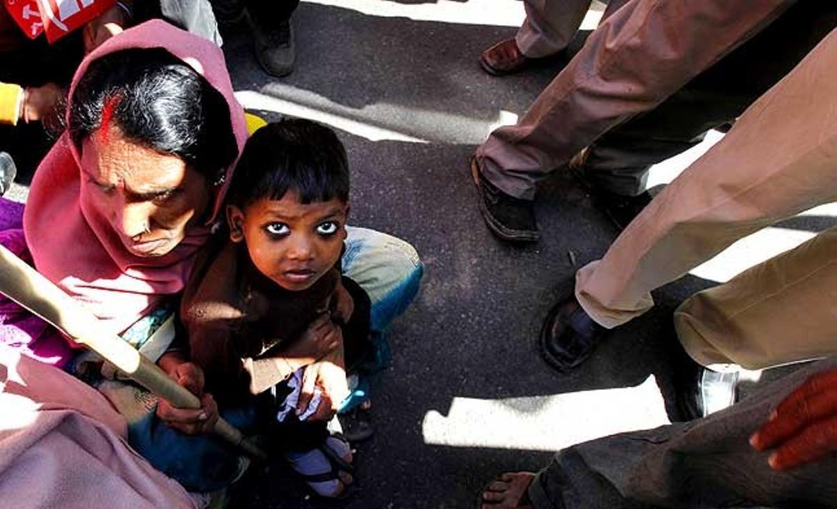 Un nen aguanta un cartell mentre està assegut a sobre de la seva mare, en una manifestació contra la pujada dels preus dels productes bàsics a Nova Delhi (Índia).