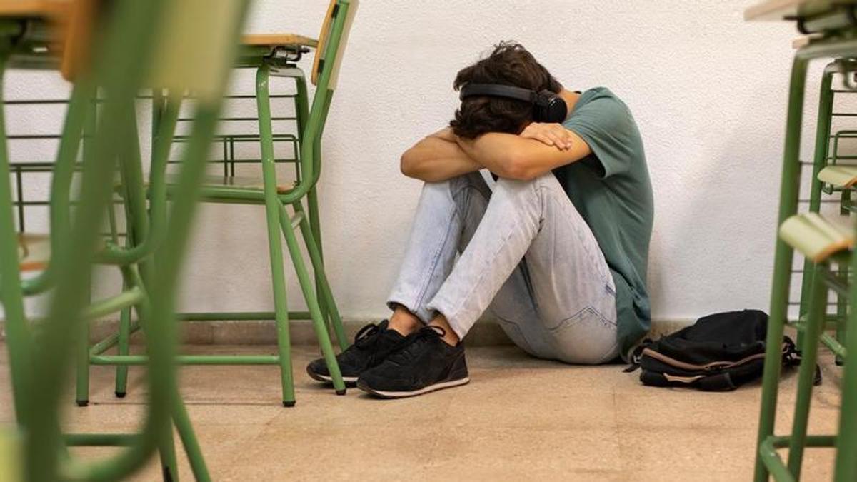 Un estudiante con auriculares en el suelo de un aula.