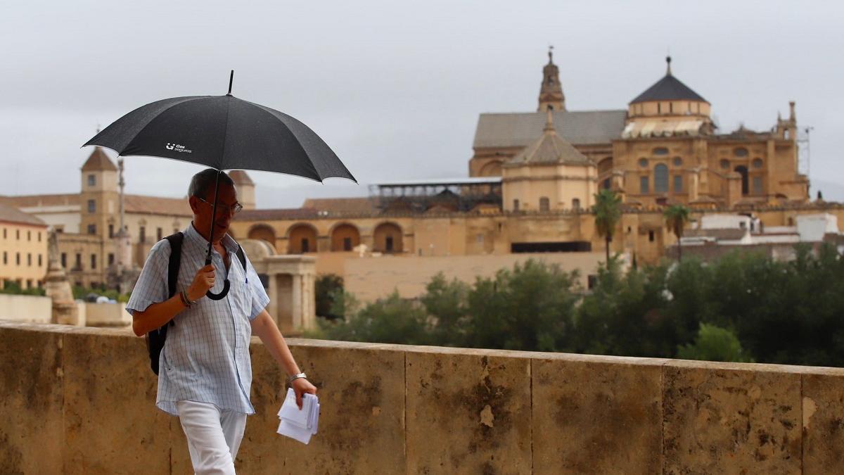 Un hombre pasea por el entorno del Puente Romano de Córdoba bajo un cielo encapotado, en Córdoba.