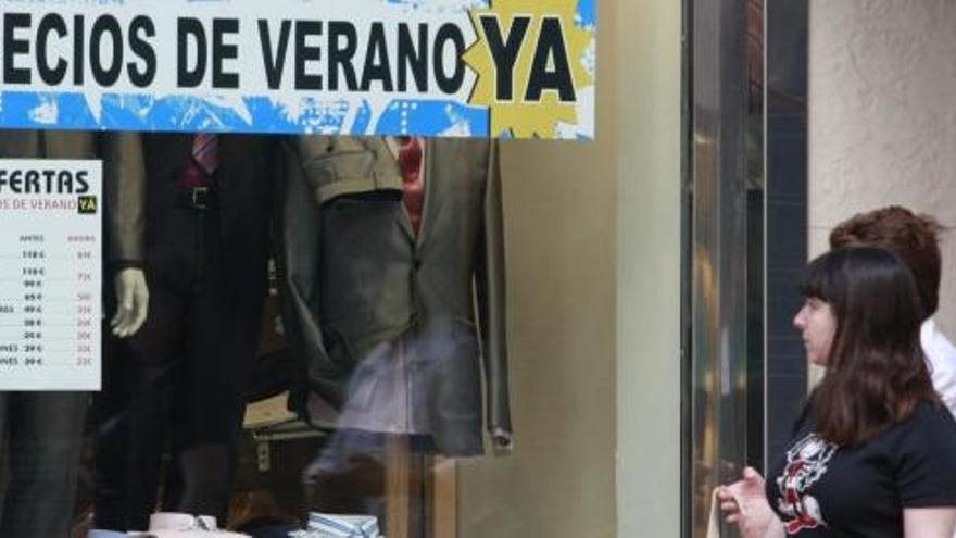 Dos jóvenes pasan ante un comercio que anuncia las ofertas de verano previas a las rebajas.