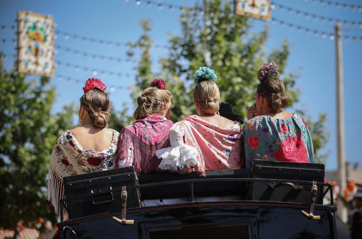 Cuatro mujeres vestidas de flamenca pasean en un coche de caballo.