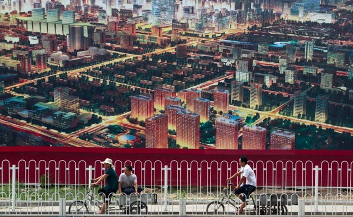 Ciclistes al seu pas per un cartell que anuncia la construcció d’un nou centre de negocis a Pequín, Xina.