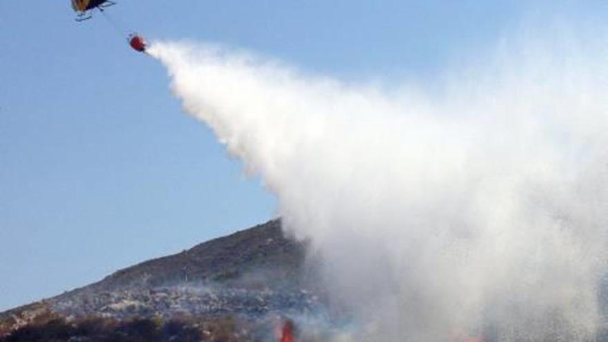 fuego en la muntanya gran.Las llamas se fueron alejando del pueblo, aunque su parte más alta quedó envuelta en humo.Un helicóptero descarga sobre el frente del incendio. Una joven observa las llamas desde su casa.