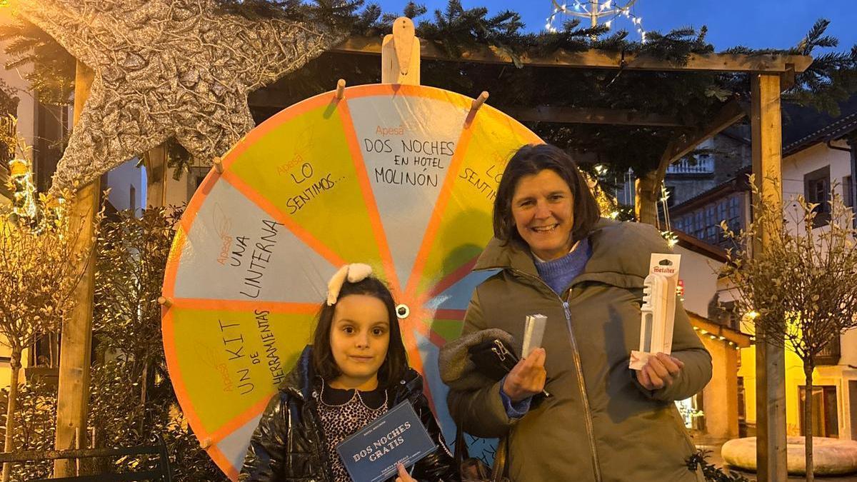 La pequeña Estela posa con el premio grande, mientras Lucía Barreiro muestra el afilador de cuchillos conseguido en la ruleta.