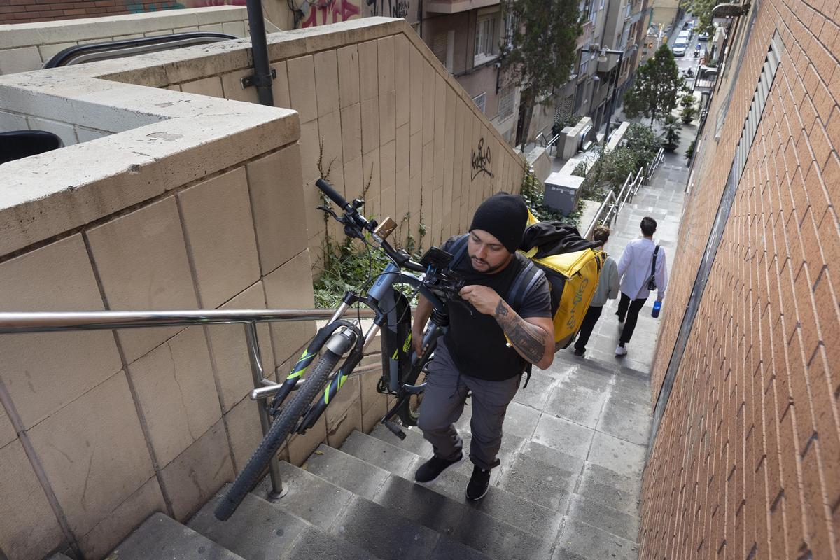 Un chico sube a peso una bicicleta junto a un tramo averiado de escalera mecánica en la Baixada de la Glòria, en el distrito de Gràcia de Barcelona.