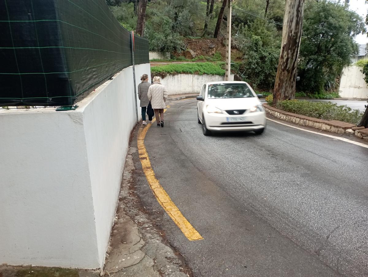 Dos personas se ven obligadas a caminar por la calzada en un tramo de la avenida de San Antón con el muro renovado hace poco y sin retranquear.
