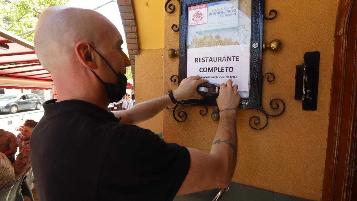Óscar, del restaurante Doña Taberna, cuelga el cartel del completo en su negocio de la avenida de Juan XXIII.