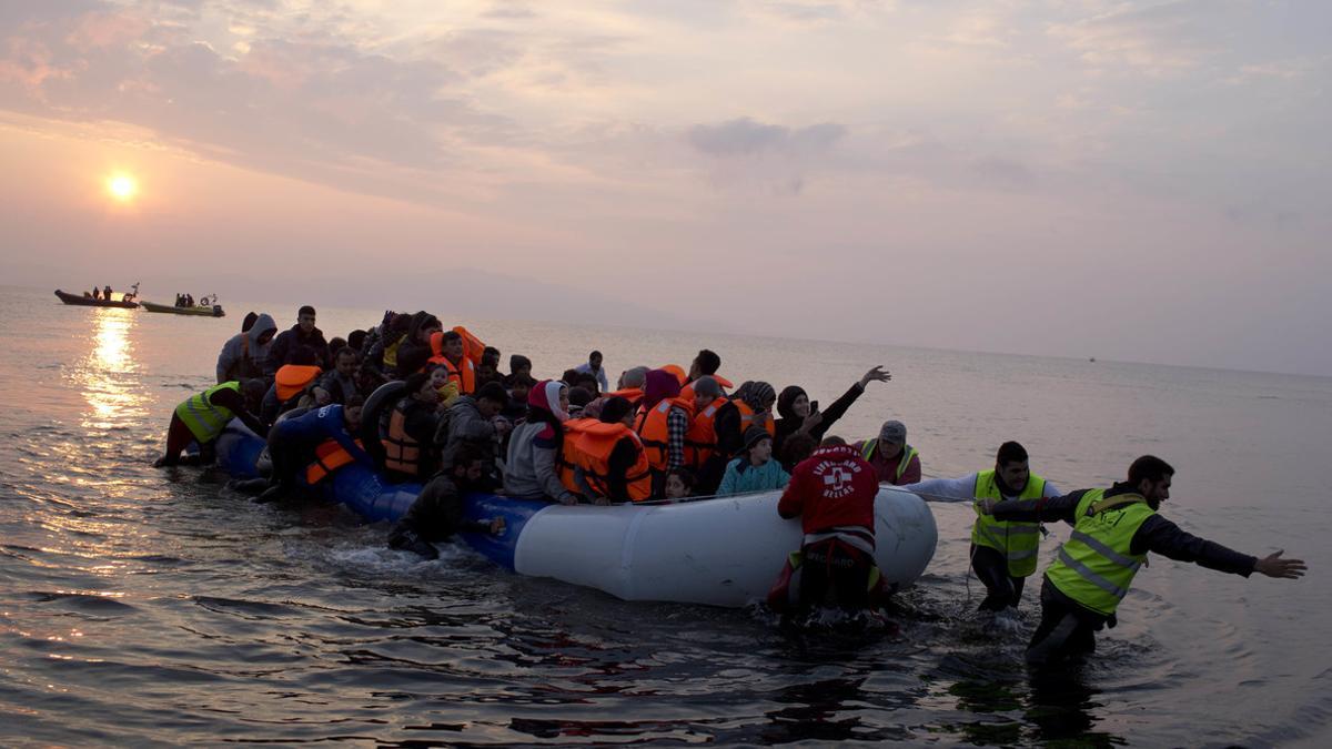 Varios voluntarios ayudan a un grupo de refugiados a llegar a la costa, en la isla griega de Lesbos.
