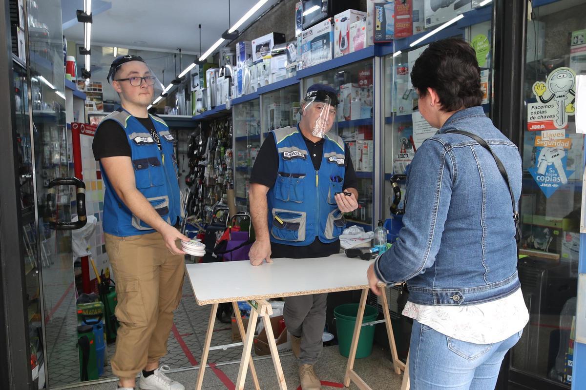 Dos empleados de la ferretería atienden a una mujer, en la misma entrada del local, durante la pandemia de covid.