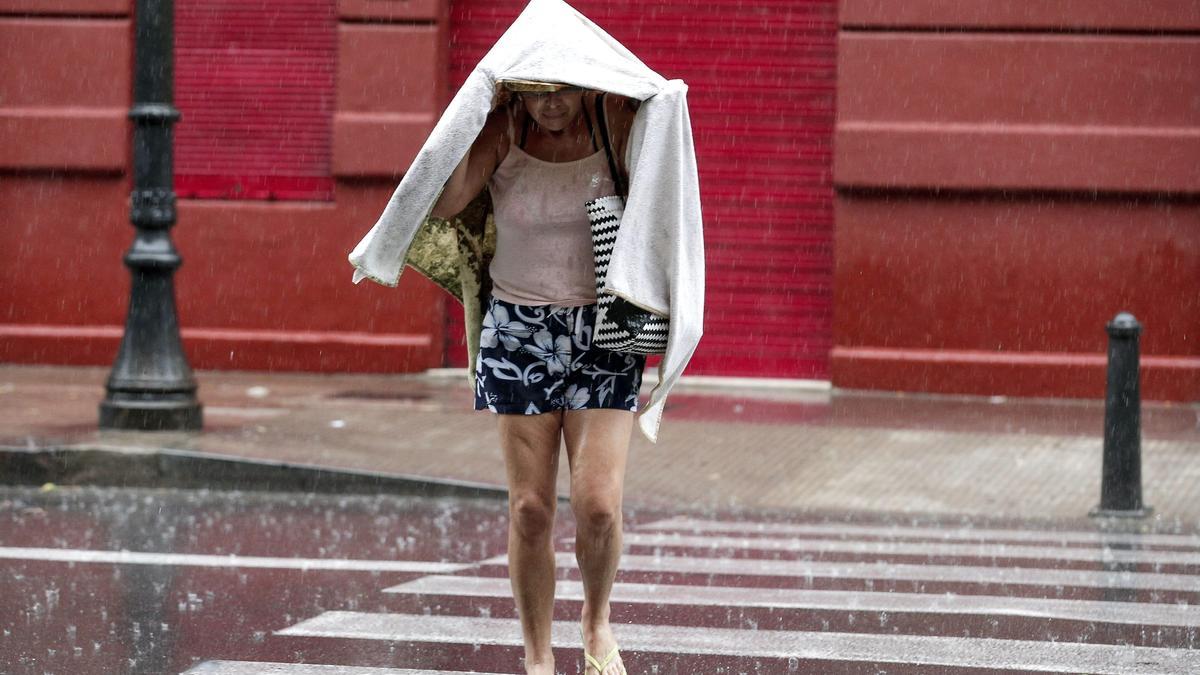 Una peatón se cubre la cabeza con una chaqueta para no mojarse.