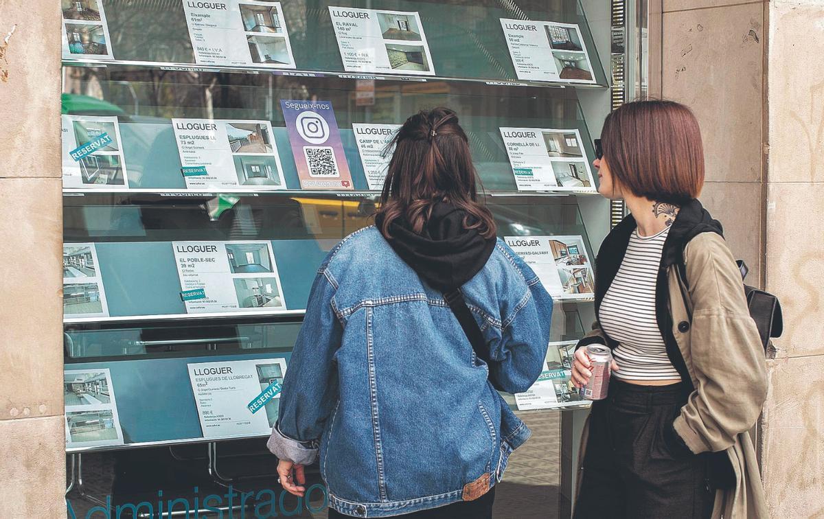 Dos jóvenes observan anuncios de pisos de alquiler en Barcelona.