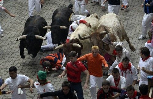 Un corredor queda atrapado entre los toros a la entrada de la plaza de toros durante el cuarto encierro de las fiestas de San Fermín en Pamplona.