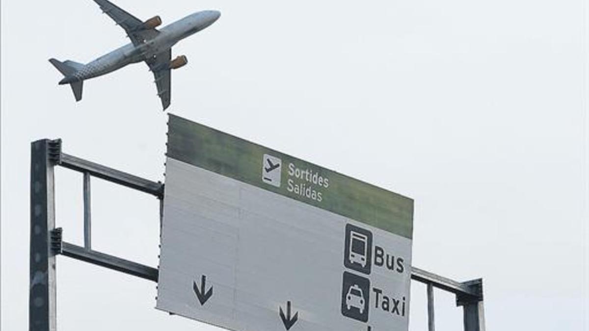 Un avión sobrevuela una de las señales de los accesos al aeropuerto de Barcelona.