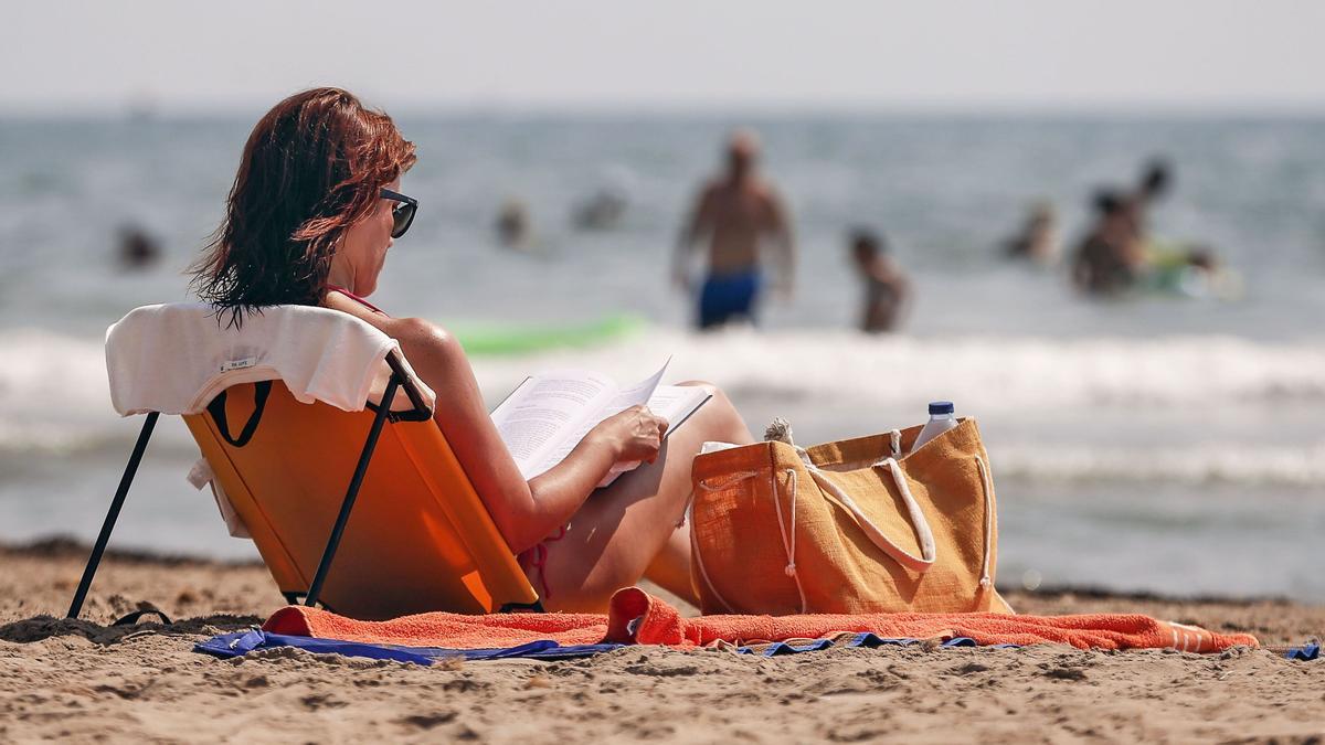 una mujer lee un libro este mediodía en la playa.