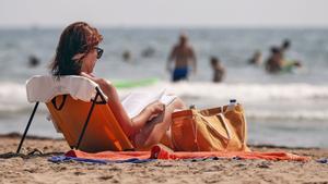 Una mujer lee un libro en una playa.