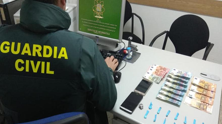 un agente de la Guardia Civil de Valga muestra la droga y el dinero intervenido al vecino de Rianxo