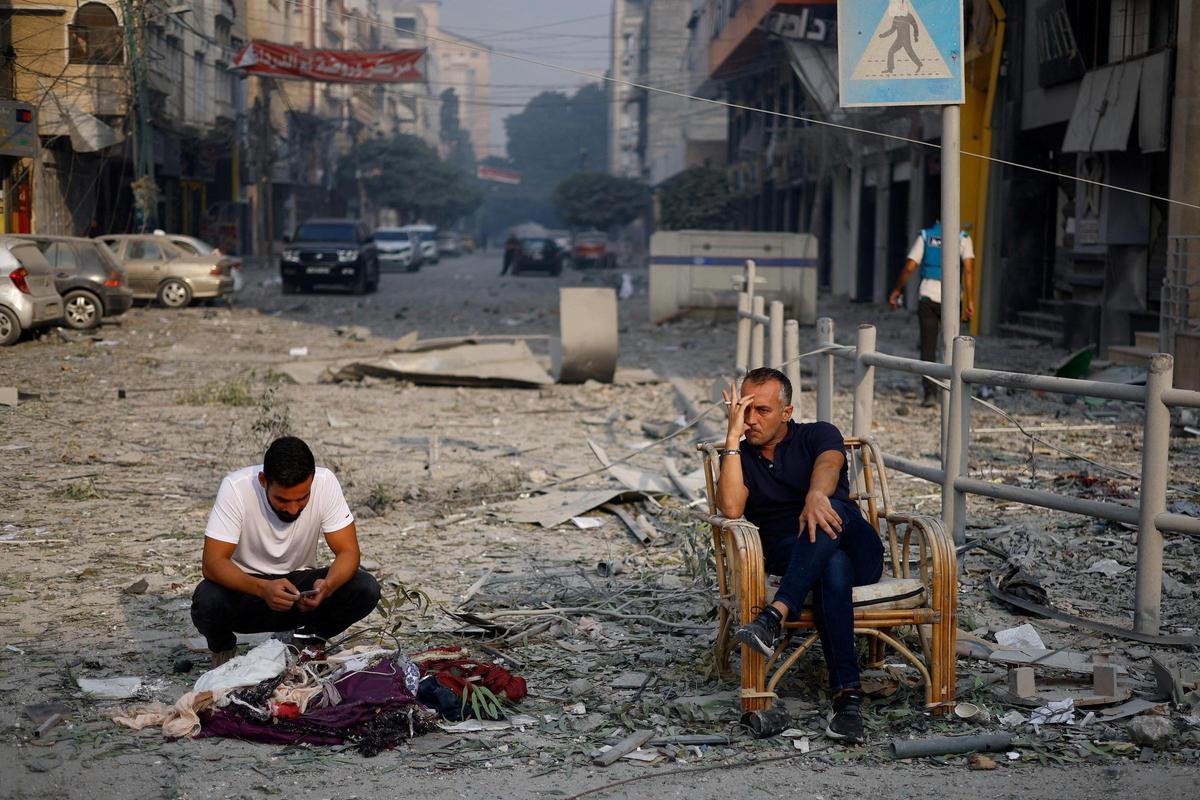 Dos palestinos se sientan en la calle, llena de escombros, cerca de la torre de Al-Watan, en Gaza, destruida por los ataques de Israel.