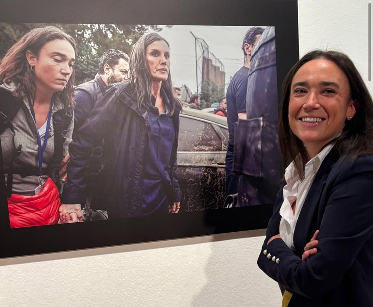 La periodista Angie Calero posa en 2025 junto a una foto en la exposición 'Letizia, de princesa a reina'. En la imagen, junto a la reina Letizia en Paiporta, durante la primera visita de los reyes durante la dana.