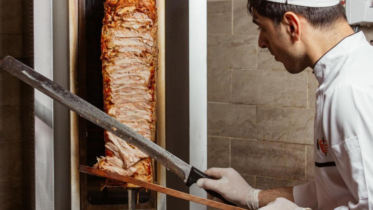 Un cuiner talla un döner de carn en un rositdor vertical