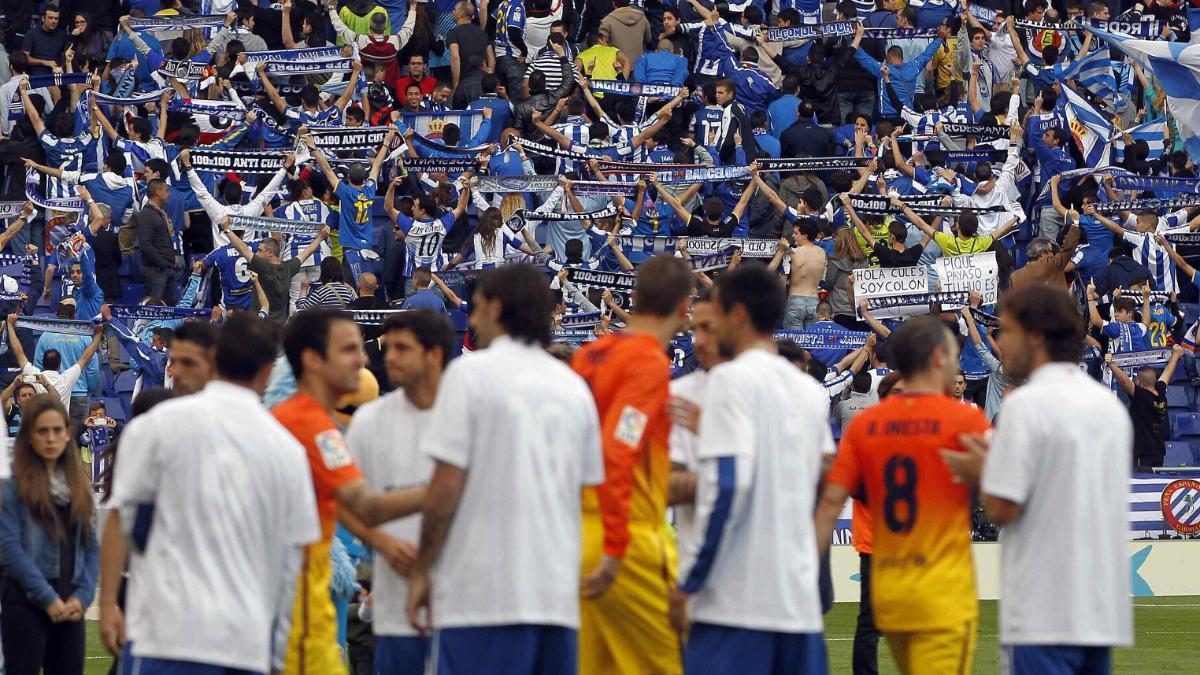 Los jugadores del Espanyol hacen pasillo a los del Barça con seguidores blanquiazules dando la espalda al campo