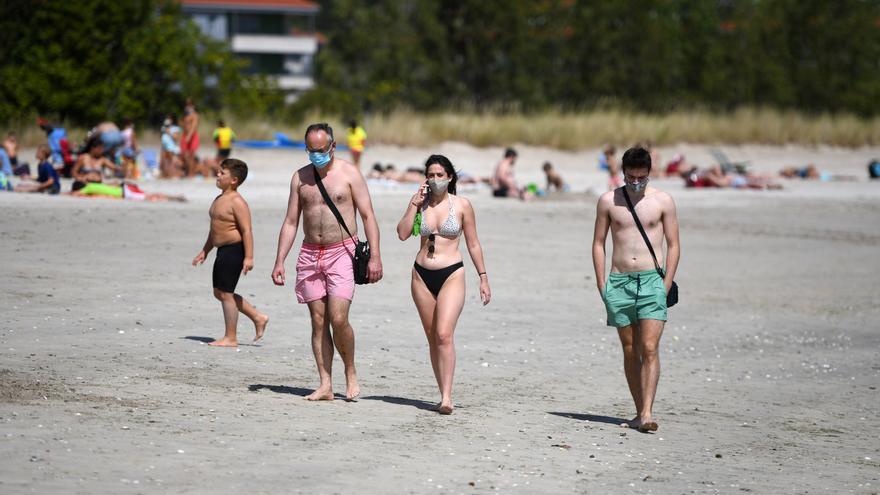 Paseantes con mascarilla en la playa.