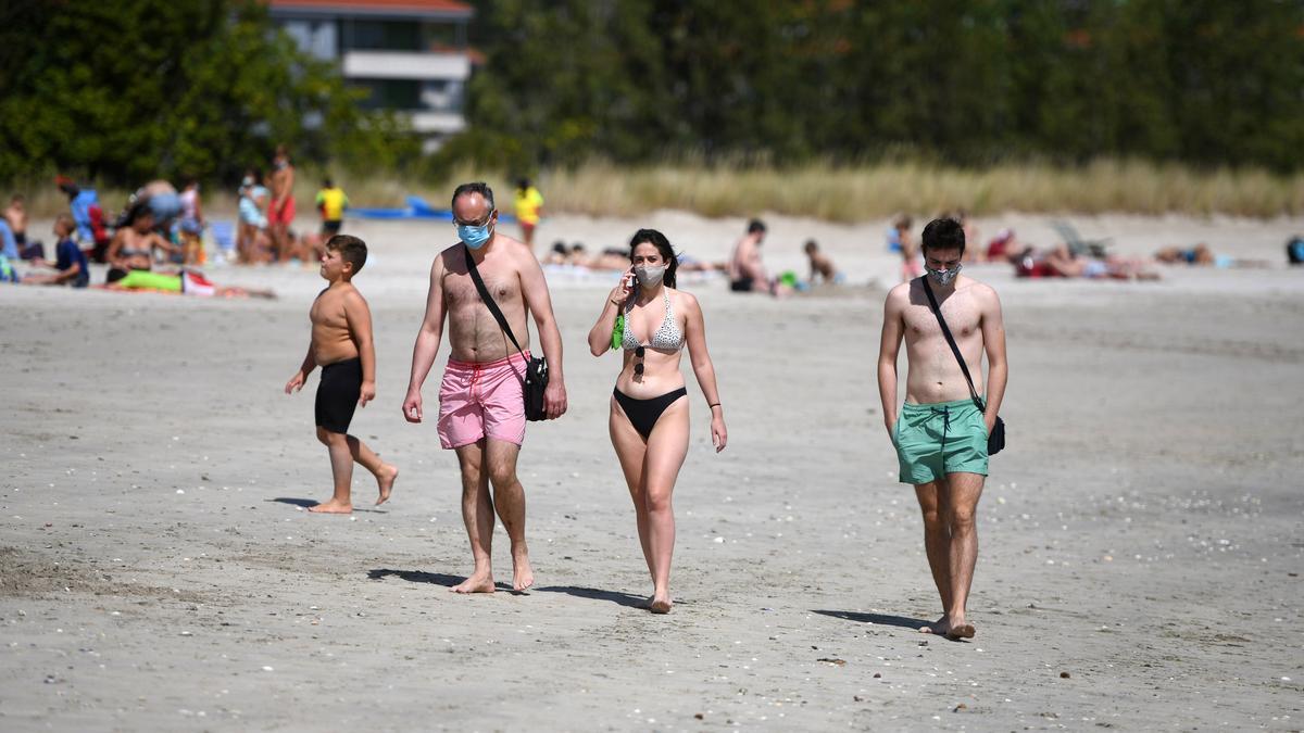 Paseantes con mascarilla en la playa.