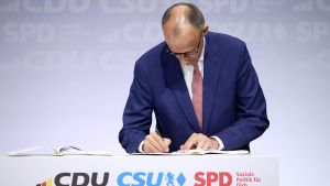 El futuro canciller alemán, Friedrich Merz, firma el acuerdo de gobierno entre CDU, CSU y SPD, este lunes en Berlín.