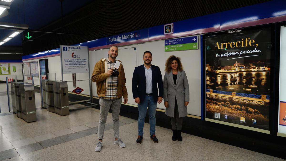 Juan Méndez, Yonathan de León y Eli Merino, junto al cartel promocional de Arrecife en la parada de metro Feria de Madrid.
