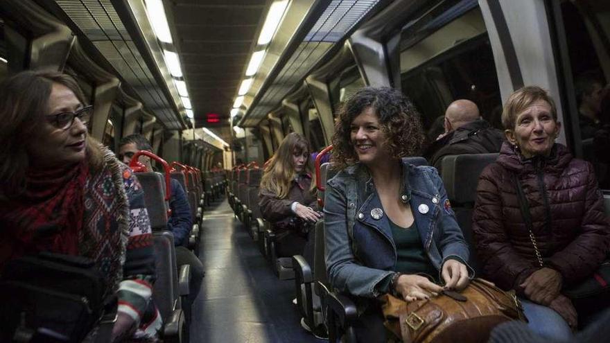 Sofía Castañón, sentada junto a Pilar Martínez, saluda a una usuaria del tren entre Moreda y Collanzo.