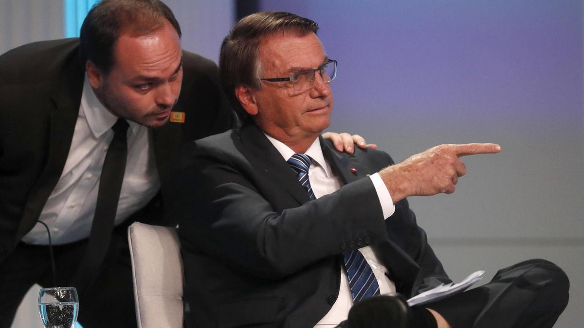Carlos Bolsonaro habla al oído a su padre antes de un debate electoral, el 29 de septiembre de 2022.