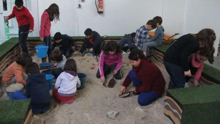 Arriba, niños excavando en la reproducción de un castro del Arqueocampo. A la derecha, con sus cuadernos didácticos.