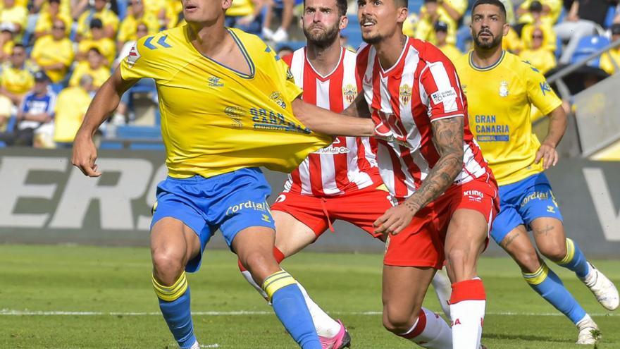 Sergi Cardona mira un centro aéreo mientras es sujetado de la camiseta por Chumi, central del Almería. | | ANDRÉS CRUZ